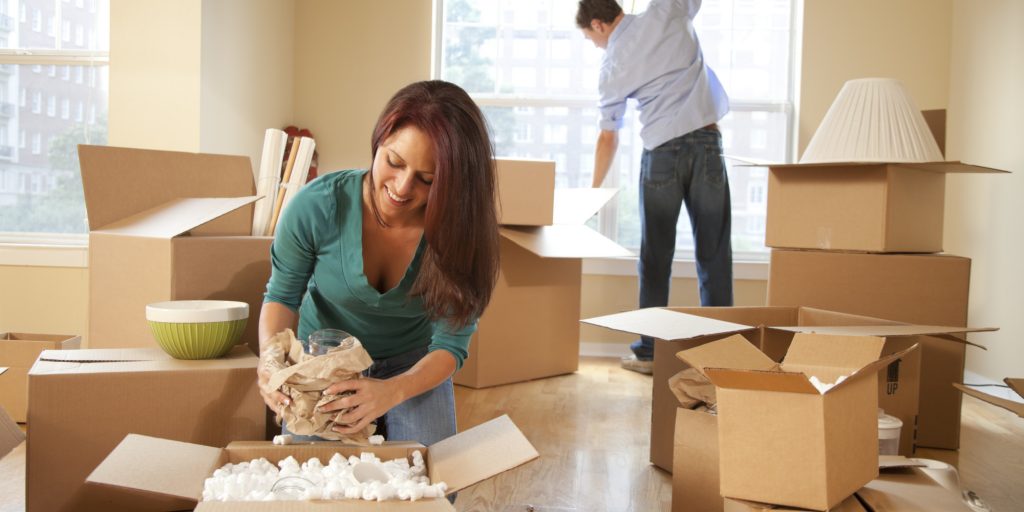 Woman unpacking glass from cardboard moving box