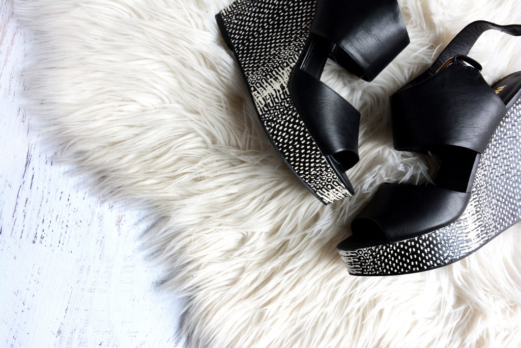 Black wedges with silver detailing on white furry carpet