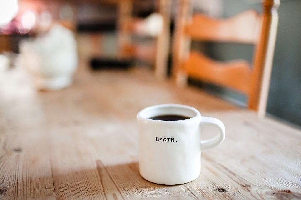 white mug with coffee on wooden table with word 'begin' 