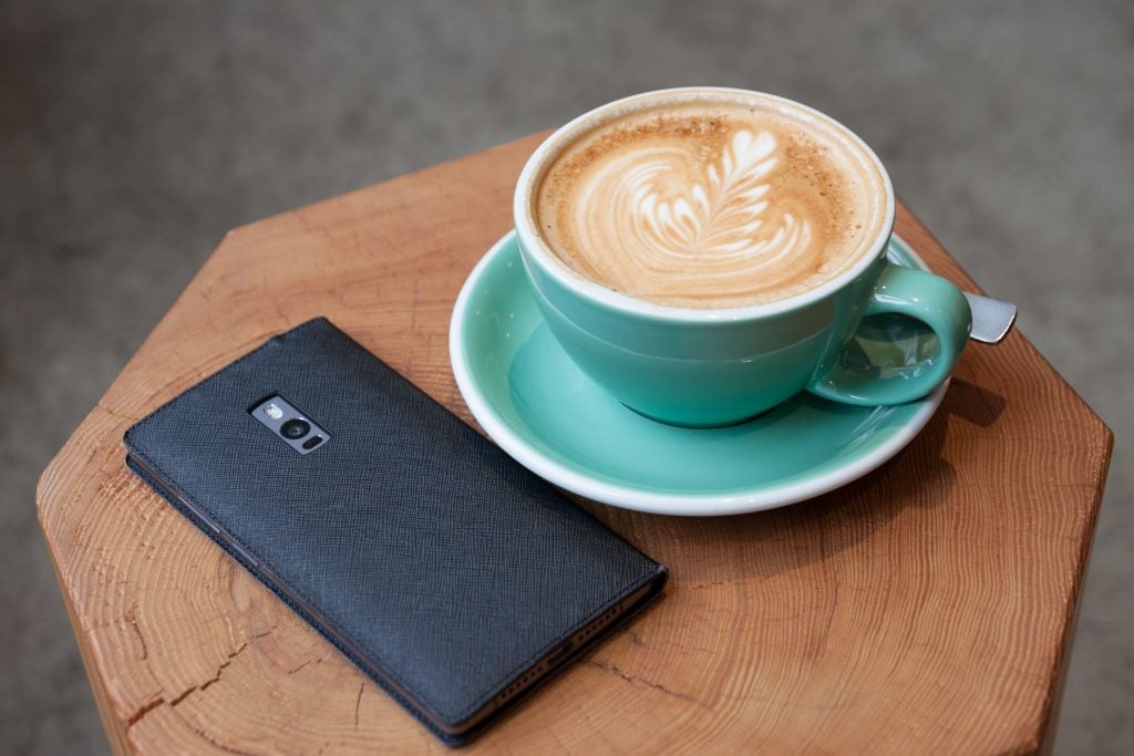 blue mug on coaster with coffee beside black smartphone 