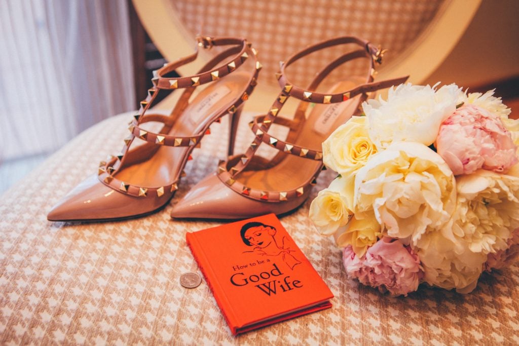 spiked high heels next to flowers and a book titled 'how to be a good wife'