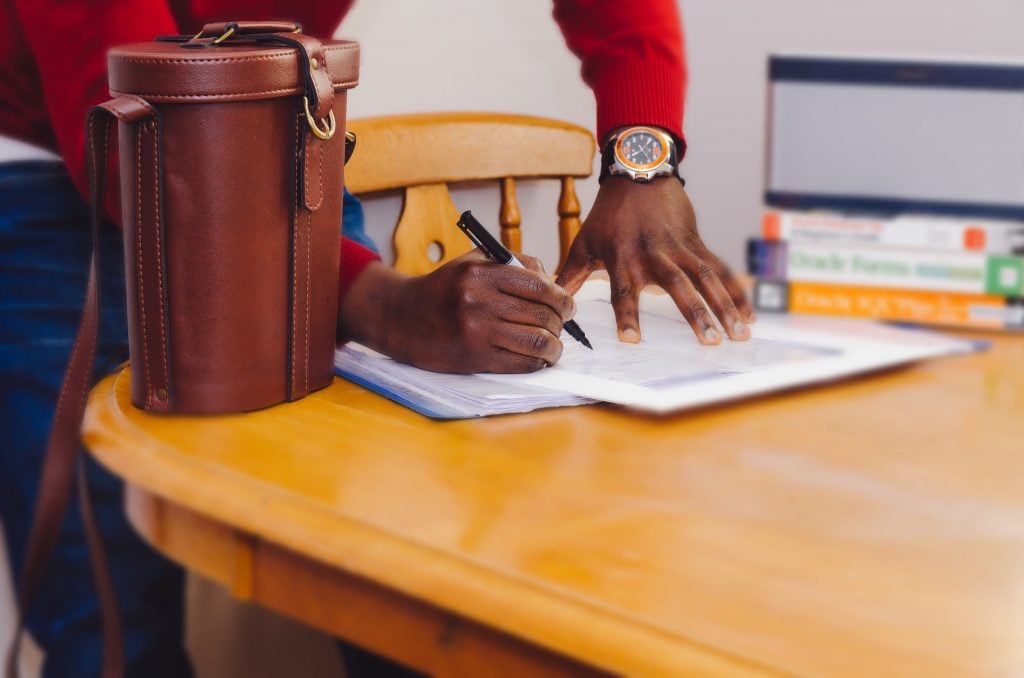 man signing contract beside brown leather bag